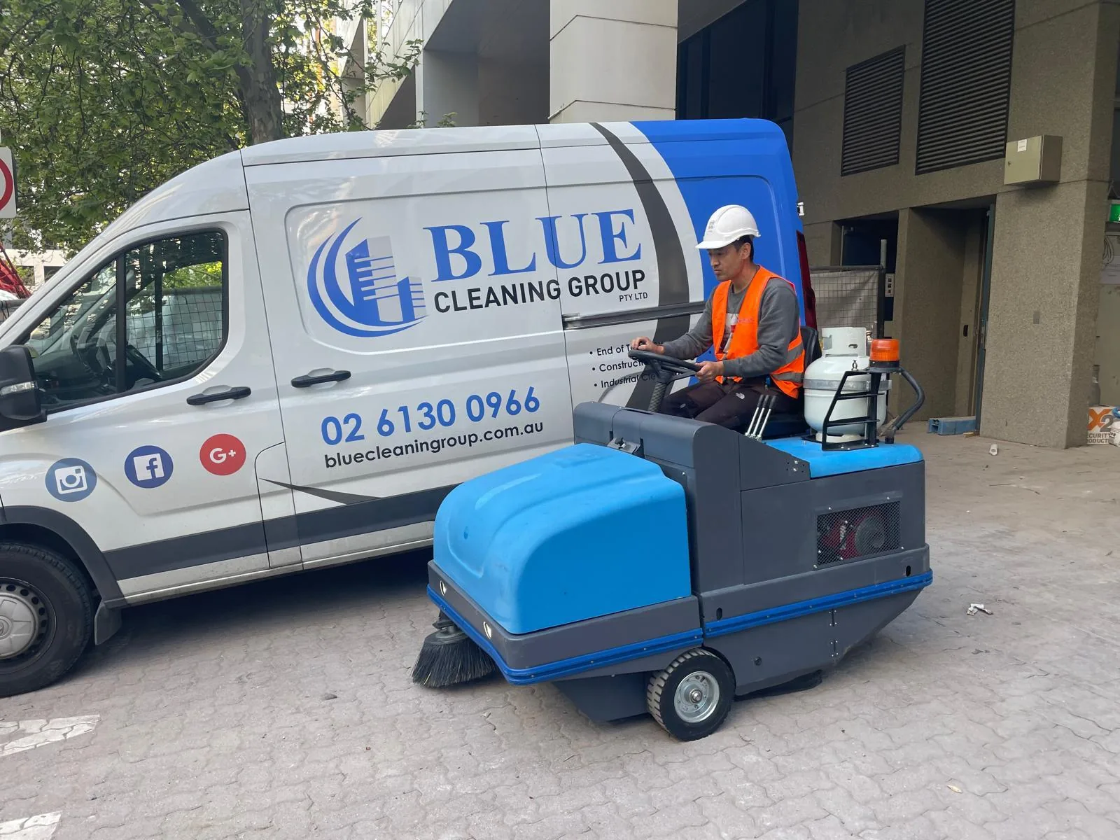 A liveried Blue Cleaning Group van parked beside a ride-on sweeper