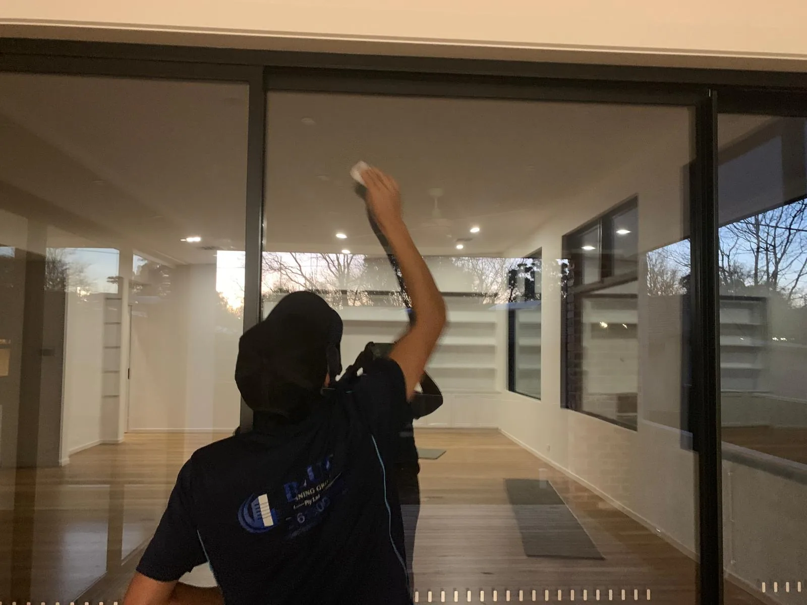 A cleaner in a back-printed Blue Cleaning Group polo wiping the inside of a full-height glass sliding door in an empty house