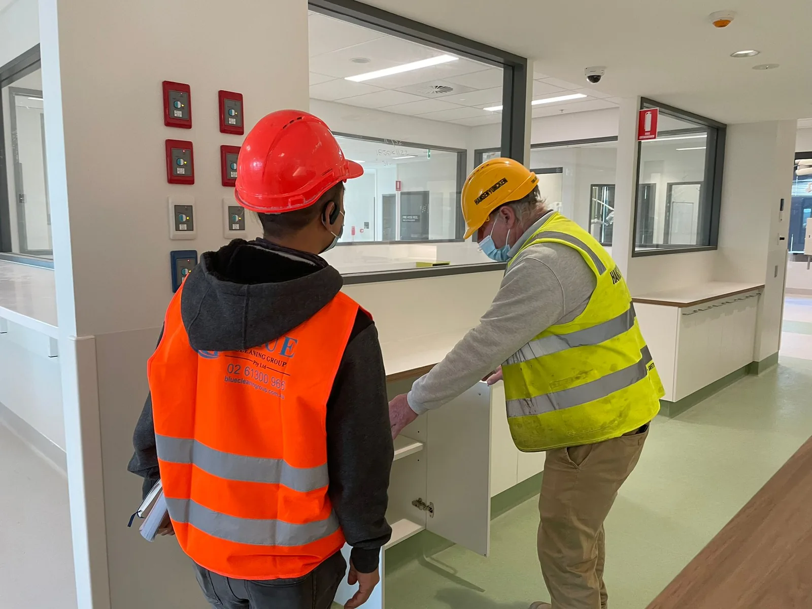 A cleaner and a builder in a hi-vis vest checking inside a joinery cabinet in a finished corridor