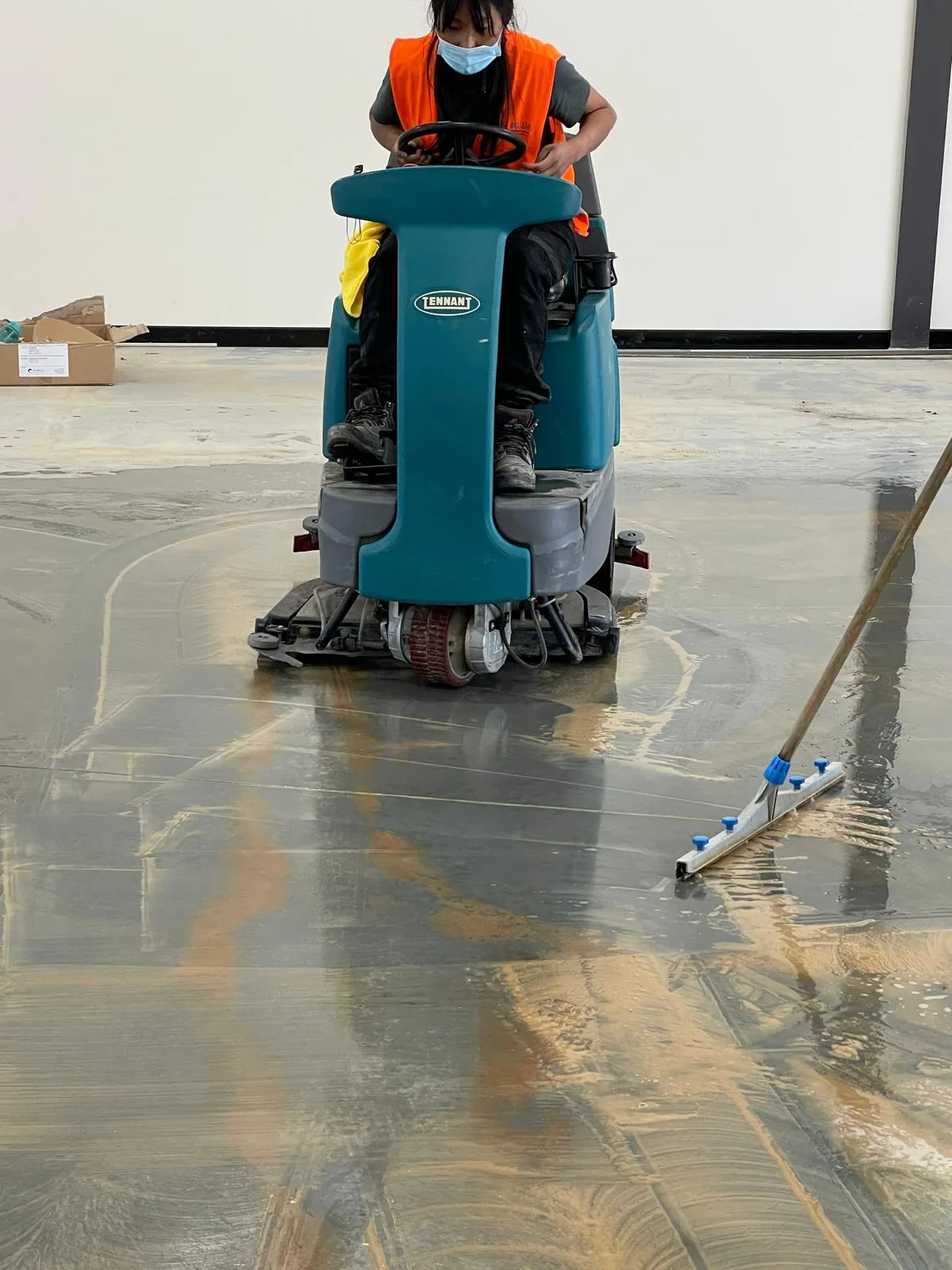 An operator on a Tennant ride-on scrubber crossing a wet concrete slab in an empty tenancy