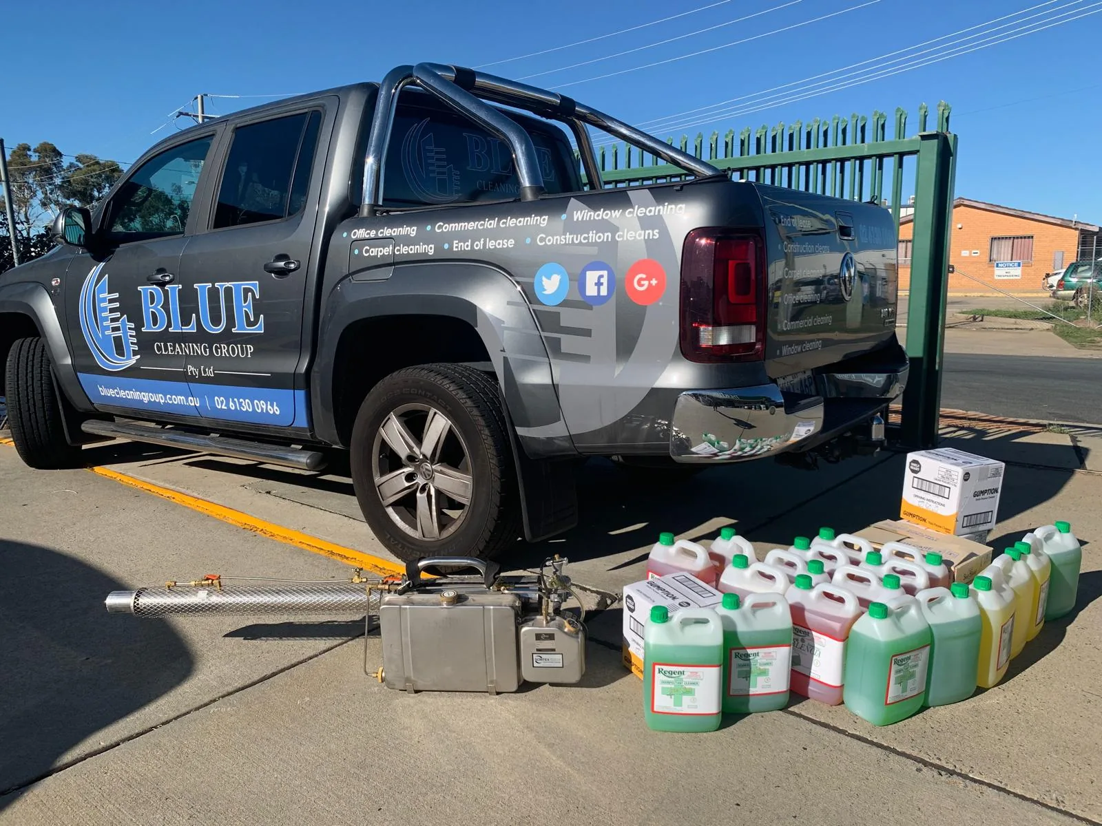 A grey signwritten Blue Cleaning Group ute in a yard, with a fogging machine and drums of disinfectant laid out in front of it