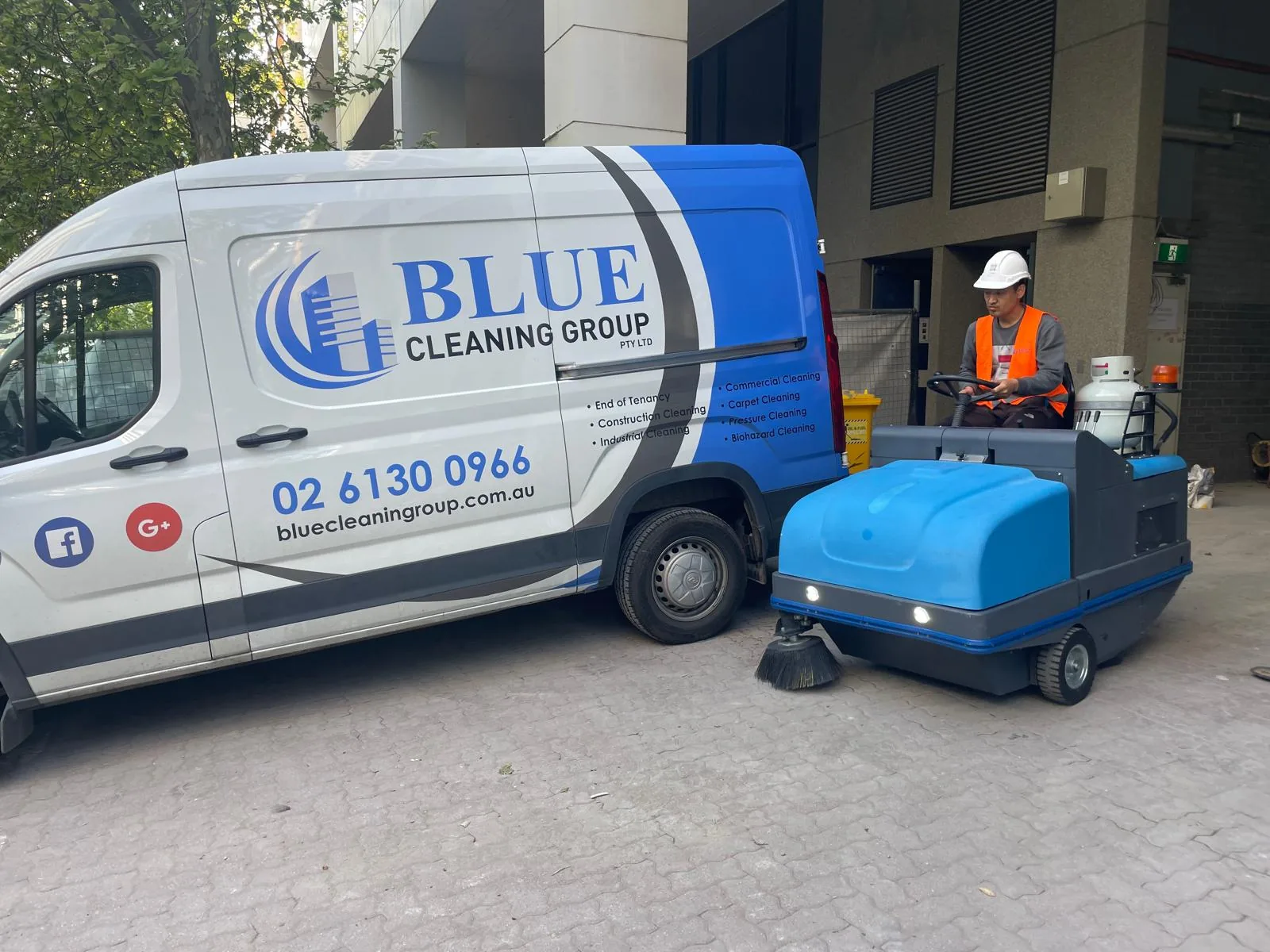 The signwritten Blue Cleaning Group van beside a ride-on sweeper and its operator in a hard hat