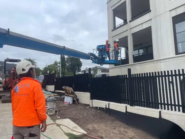 A Blue Cleaning Group spotter on the ground while two colleagues hose a render facade from a boom lift