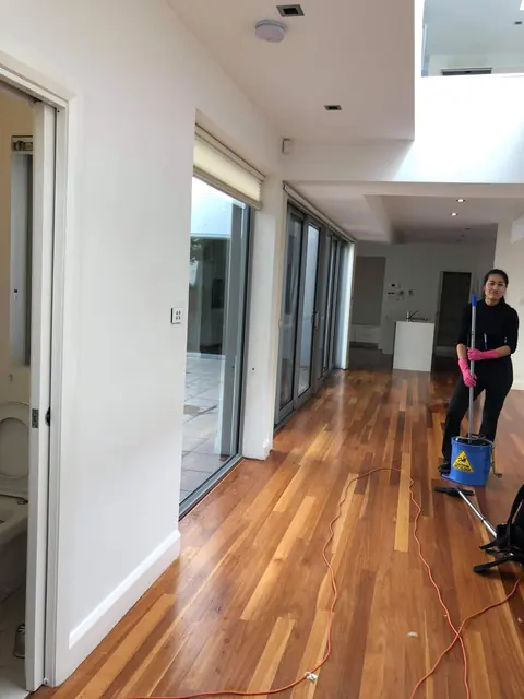 A cleaner mopping the timber floor of an emptied open-plan living area